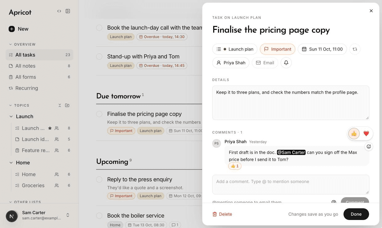 The task Finalise the pricing page copy open beside All tasks. Under the title, a row of icons: Launch plan, Important, Sun 11 Oct 11:00, repeat, Priya Shah, Email and the bell. Below the details, Priya's comment mentioning Sam Carter sits in a box with a thumbs up chip on it, and a small bar with a thumbs up and a heart is open above it.